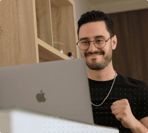 Man smiling and clenching his fist in excitement while looking at a laptop.